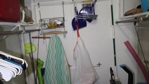 Uma lavanderia pequena com varal, tábua de passar e diversos produtos de limpeza.