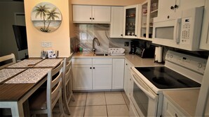 Uma cozinha moderna com armários brancos, micro-ondas embutido, fogão e uma área de jantar com mesa e cadeiras.