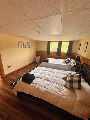 A bedroom with two beds, a wooden floor, a ceiling with a security camera, and a window with curtains. - Paugus Bay Cottage waterfront cottage on private island! (Laconia)