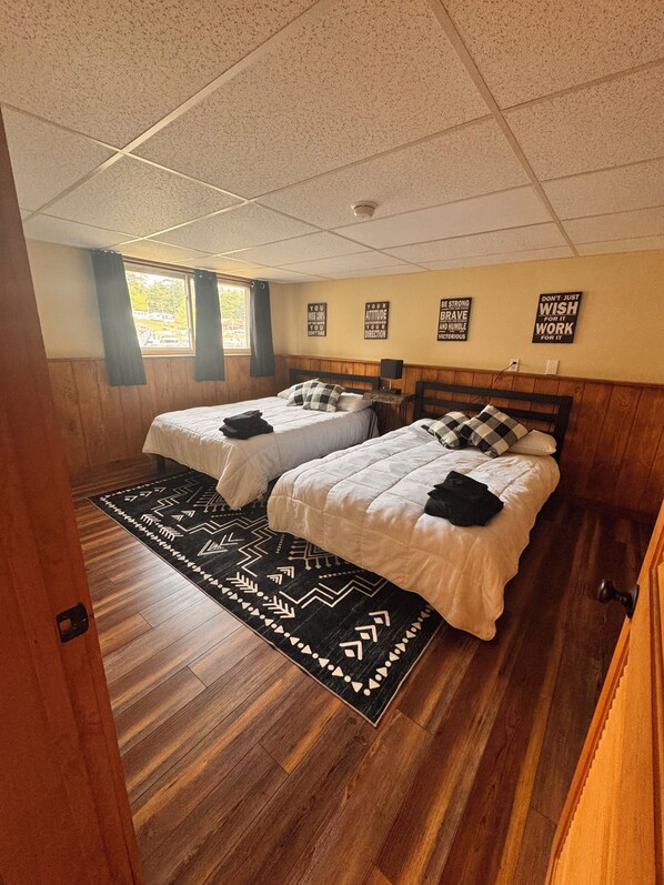 A room with two beds, a patterned rug, wooden flooring, and motivational wall art.