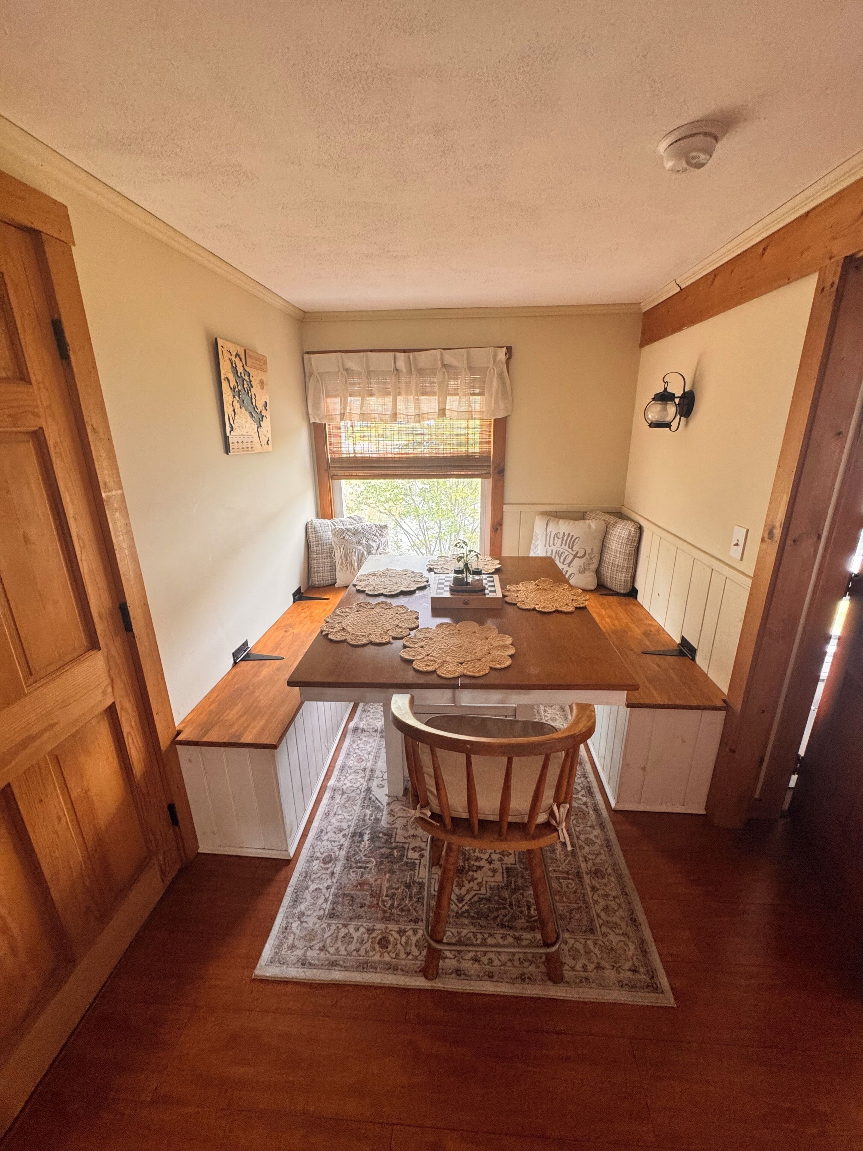 Un coin repas avec une table en bois, des bancs, un tapis à motifs et une fenêtre donnant sur un paysage agréable.