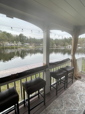 A covered outdoor seating area with a view of a lake and houses in the background.