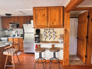 Una cocina con armarios de madera, microondas, cafetera y una barra de café con tazas.