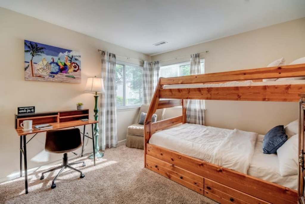 A bedroom with a wooden bunk bed, a desk with a chair, a lamp, and a painting on the wall.