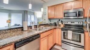 Una cocina moderna con encimeras de granito, electrodomésticos de acero inoxidable, armarios de madera e iluminación colgante.