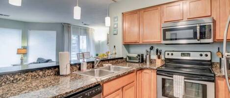 A modern kitchen with granite countertops, stainless steel appliances, wooden cabinets, and pendant lighting.