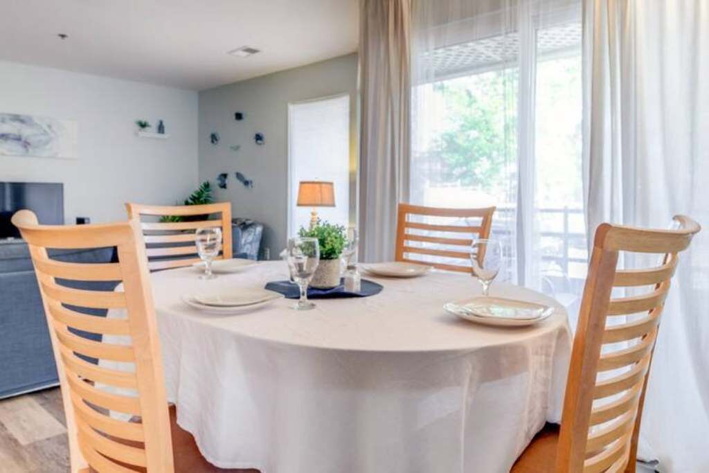 Un coin repas avec une table ronde dressée pour quatre personnes, entourée de chaises en bois.