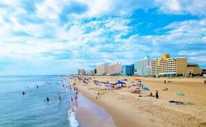 Una playa con gente, sombrillas y edificios al fondo.