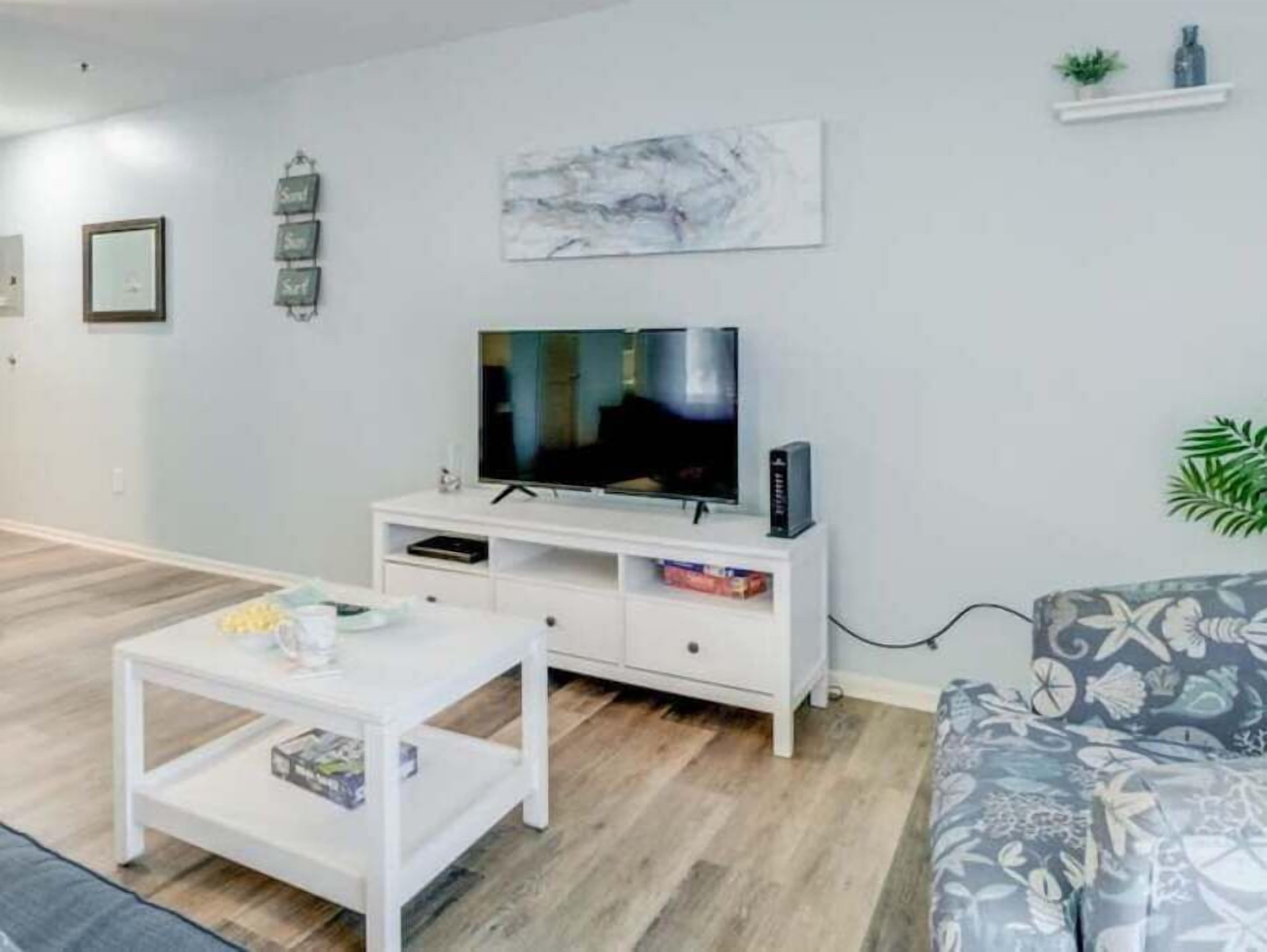A modern living room with a flat-screen TV on a white entertainment unit, a coffee table, and a patterned sofa.