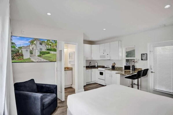 A modern kitchen with white cabinets, a countertop, and a dining area with a white table and black chairs.