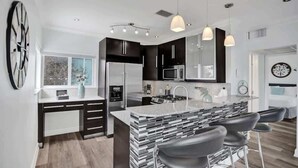 Una cocina moderna con una isla central, armarios negros, electrodomésticos de acero inoxidable e iluminación colgante.