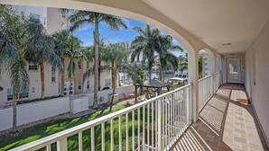 A balcony with a view of a courtyard, palm trees, and a building in the background. - Modern 1BR on 2nd Floor Near Las Olas (Fort Lauderdale)