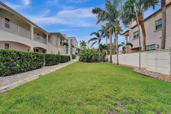 A courtyard with a well-maintained lawn, palm trees, and a pathway leading to a building with balconies.