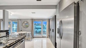 A modern kitchen with a stainless steel refrigerator, a marble countertop, and a dining area with a view through large glass doors. - Modern 1BR Waterfront Stay w/ Patio | Las Olas (Fort Lauderdale)