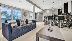 A modern living room with a sofa, a coffee table, and a kitchen area with a stone backsplash. - Modern 1BR Waterfront Stay w/ Patio | Las Olas (Fort Lauderdale)