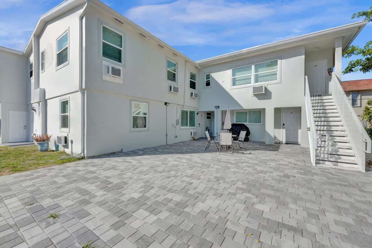 Un bâtiment moderne à deux étages, doté d’une cour dallée, d’un espace extérieur aménagé pour s’asseoir et d’un escalier menant à l’étage supérieur.