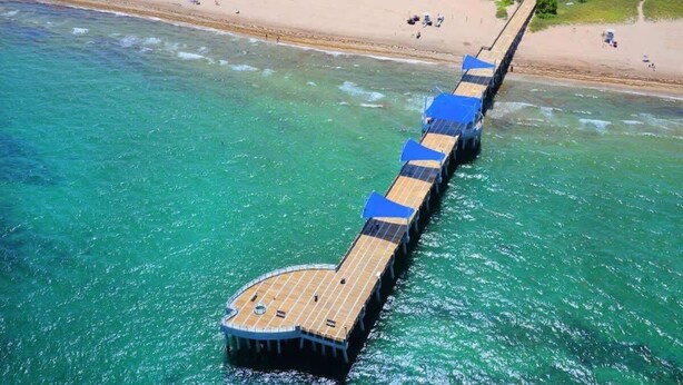 An aerial view of a pier extending into turquoise waters with a beach in the background.