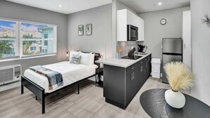 A modern bedroom with a bed, a small desk, and a kitchenette.