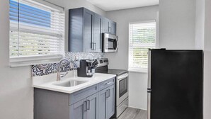 A modern kitchen with grey cabinets, a stainless steel microwave, a black refrigerator, and patterned backsplash tiles. - Urban Escape 1BR Near Las Olas (Fort Lauderdale)