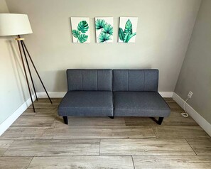Un canapé gris placé dans un coin, avec un lampadaire et trois œuvres d’art murales représentant des motifs de feuilles.