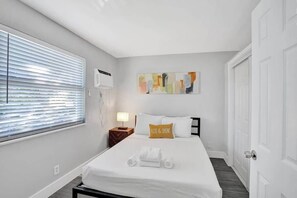Ein Hotelzimmer mit einem großen Bett, einem Nachttisch mit Lampe, einem Fenster mit Jalousien und einem Bild an der Wand.
