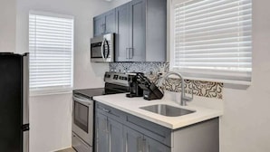 A compact kitchen with grey cabinets, a stainless steel microwave, a stove, and a coffee maker.