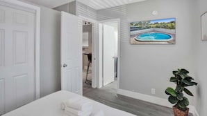 A bedroom with a bed, a potted plant, and a framed picture of a swimming pool.