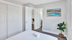 Un dormitorio con una cama, una planta en maceta y un cuadro de una piscina.