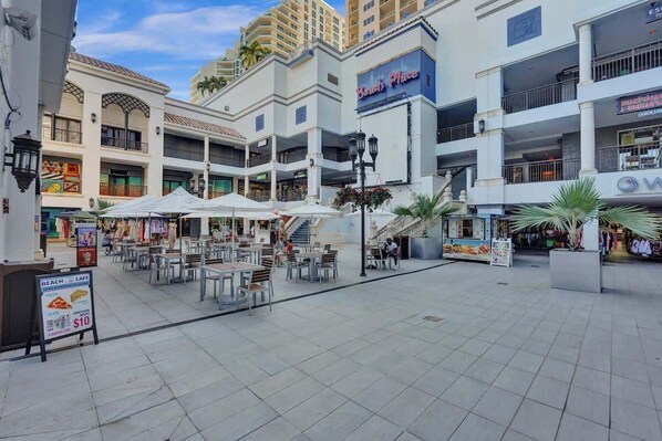 A multi-level shopping mall with outdoor seating areas and various retail stores.