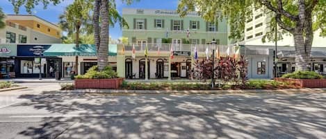 Un hotel con fachada verde, varias banderas y una entrada central con porche cubierto.