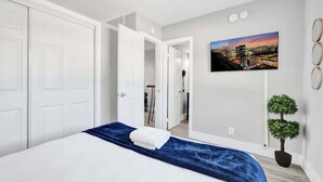 A modern hotel room with a large bed, a cityscape painting, and a small potted plant. - Urban Escape 1BR Near Las Olas with  Pool (Fort Lauderdale)