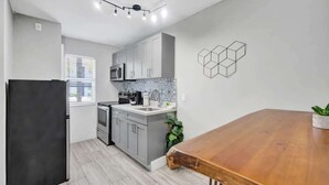 A modern kitchen with grey cabinets, a black refrigerator, and a wooden dining table. - Urban Escape 1BR Near Las Olas with  Pool (Fort Lauderdale)