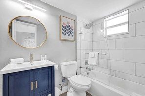 Une salle de bain moderne avec un lavabo blanc, un meuble-lavabo bleu foncé, des toilettes et une baignoire.