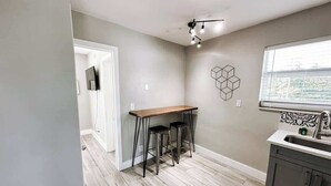 A kitchen with a wooden bar stool set, a window with a view, and a modern light fixture.