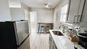 A modern kitchen with a stainless steel refrigerator, a wooden dining table with stools, a sink with a modern faucet, and decorative wall tiles.