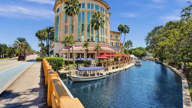 A hotel with a curved facade, a canal in front, and palm trees.