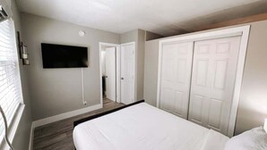 A bedroom with a large bed, a flat-screen TV mounted on the wall, and a closet with two doors.