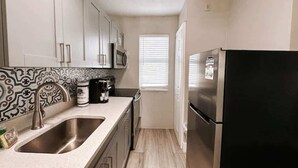 A compact kitchen with a double sink, stainless steel appliances, and a patterned backsplash.