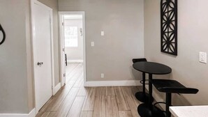 A room with a dining table and chairs, a white door, and a hallway leading to another room.