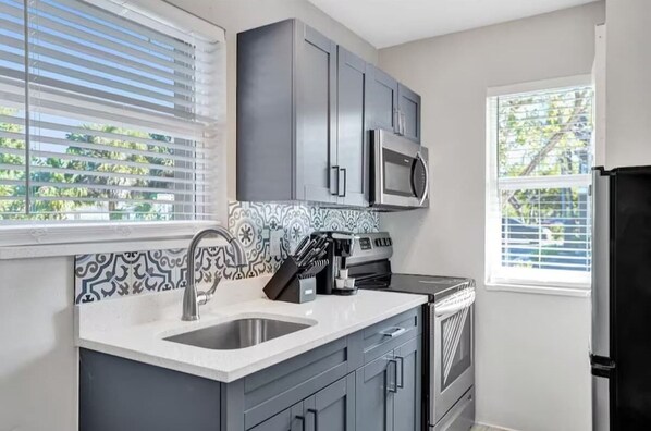 A kitchen with grey cabinets, a stainless steel sink, a microwave, and a stove.