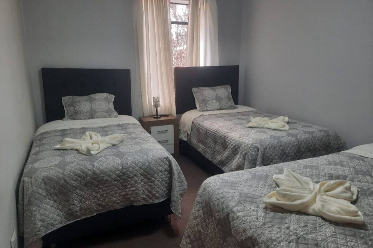 A hotel room with two single beds, each with a matching headboard and pillow, and a bedside table with a lamp.