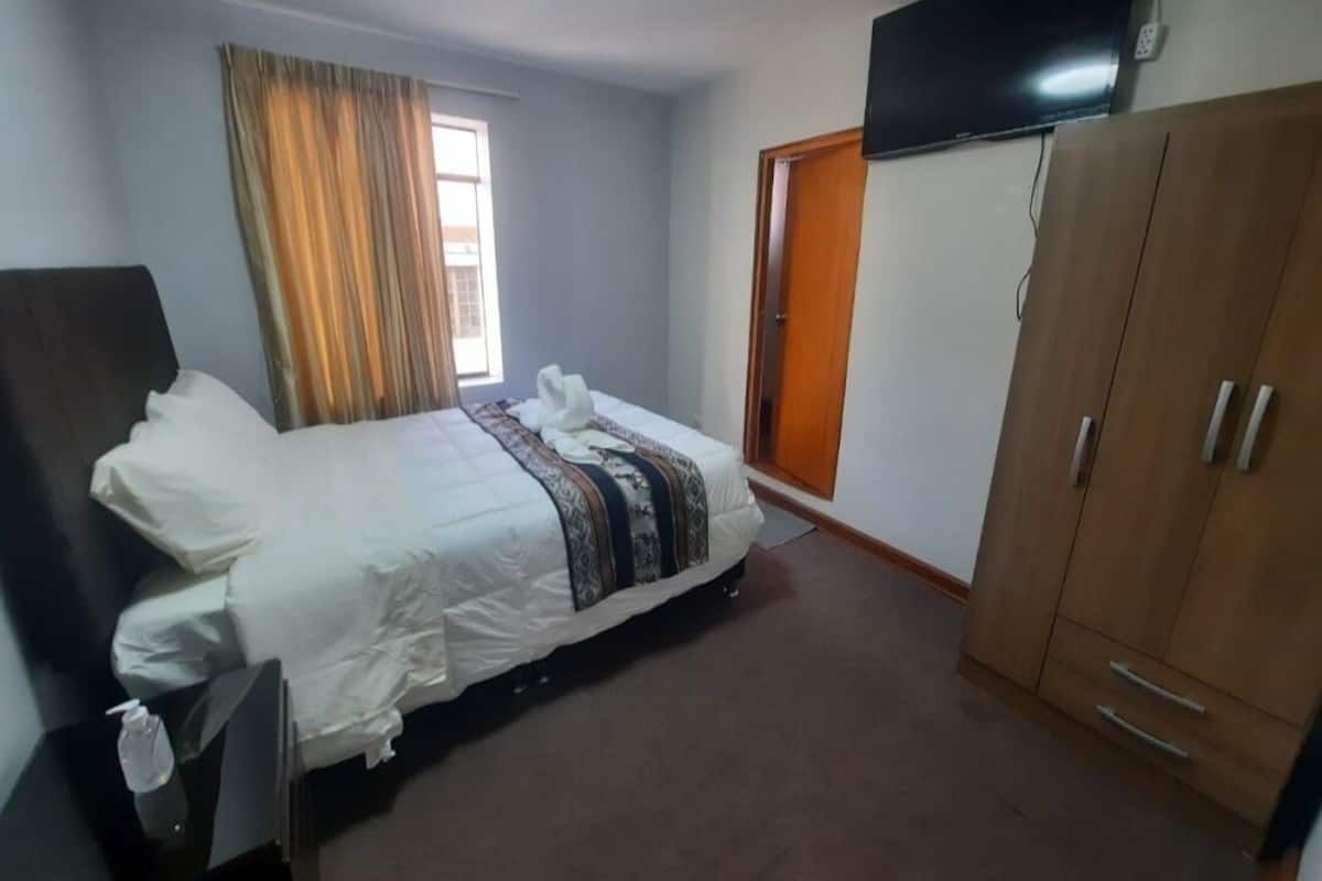 A hotel room with a bed, a wardrobe, a television mounted on the wall, and a window with curtains.