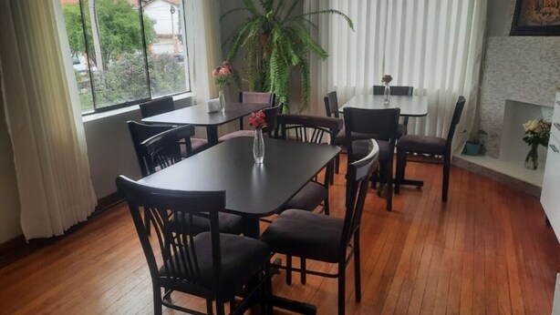 A dining area with a large table and chairs, a potted plant, and a view of the outdoors through a window. - Valícha B&B breakfast (Cusco)