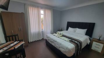 Quarto com cama, guarda-roupa, escrivaninha e janela com cortinas.