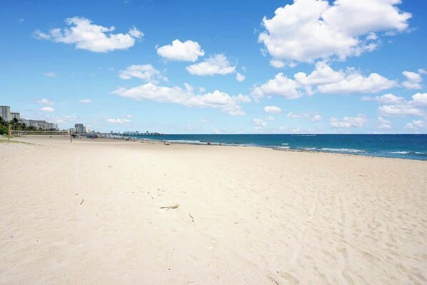 A wide sandy beach with a clear blue sky and scattered clouds.