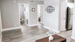 Un vaste espace de vie doté d’un plancher en bois, d’une table basse agrémentée d’un vase et d’une décoration murale hexagonale.