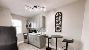 Una cocina moderna con armarios grises, un refrigerador negro, un microondas y una cafetera. Hay dos taburetes negros y un adorno en la pared.