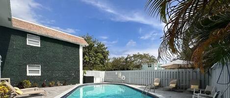 Une piscine rectangulaire dont la profondeur maximale est indiquée à 6 pieds, entourée de carreaux de pierre et agrémentée de mobilier d’extérieur.
