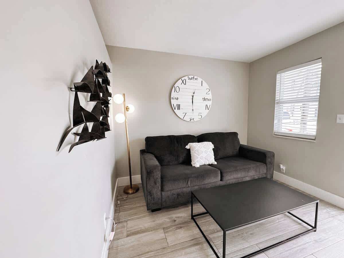 A modern living room with a grey sofa, a round wall clock, and a floor lamp.