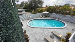 Una piscina con sillas de descanso y un área de estar cubierta, rodeada por una valla y vegetación.